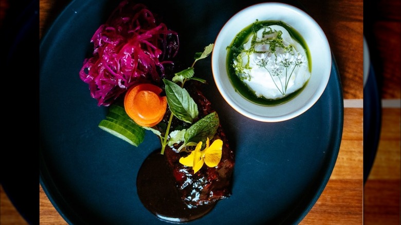 Artfully plated and garnished lamb neck with pickled cabbage, cucumber, and white sauce