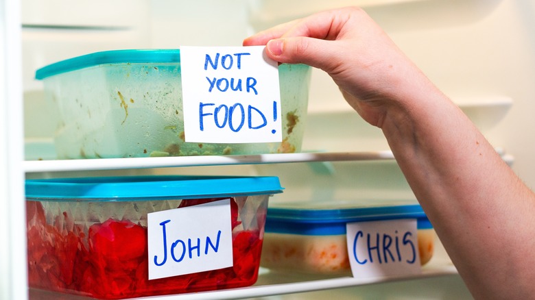 A hand reaching for a plastic container with a label that says 'not your food' in a communal fridge