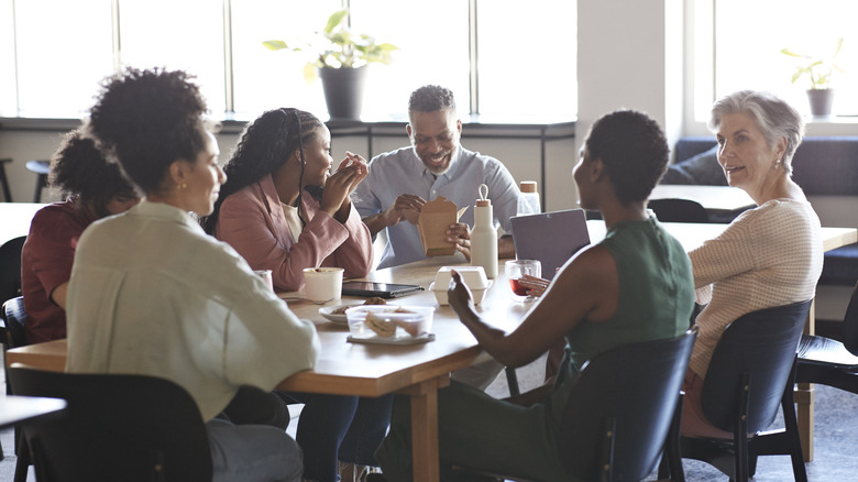 A group of work colleagues sitting around a table in the company breakroom as they eat lunch