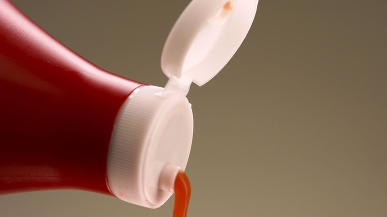 The flip top lid of a bottle of ketchup with ketchup pouring out