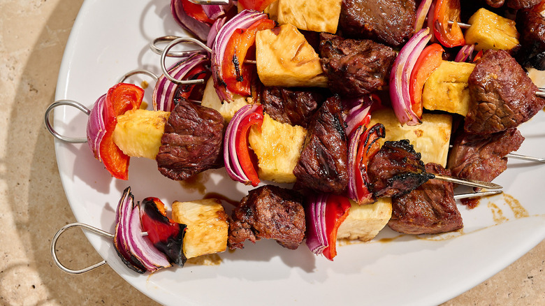 beef kabobs with peppers and pineapples on a platter