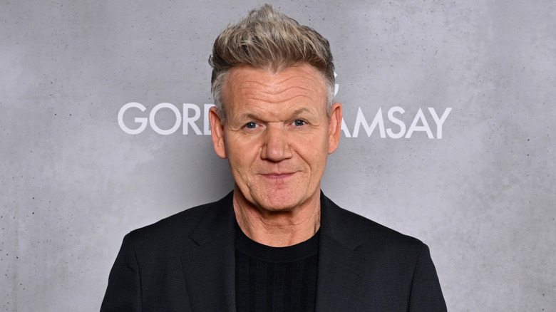 Close-up headshot of Gordon Ramsay in a black suit against gray sign