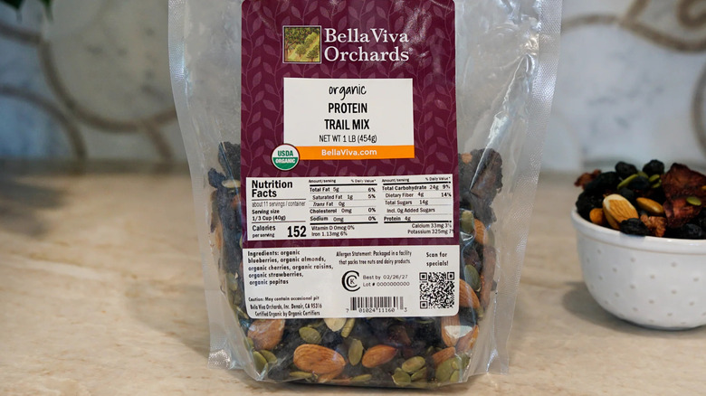 Bag of Bella Viva Orchards Protein Trail Mix with bowlful of product in background