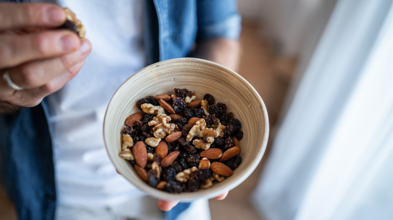 Man holding bowl of trail mix in one hand while standing and eating it