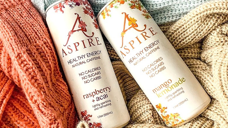 Two cans of aspire energy drinks laying on knit material