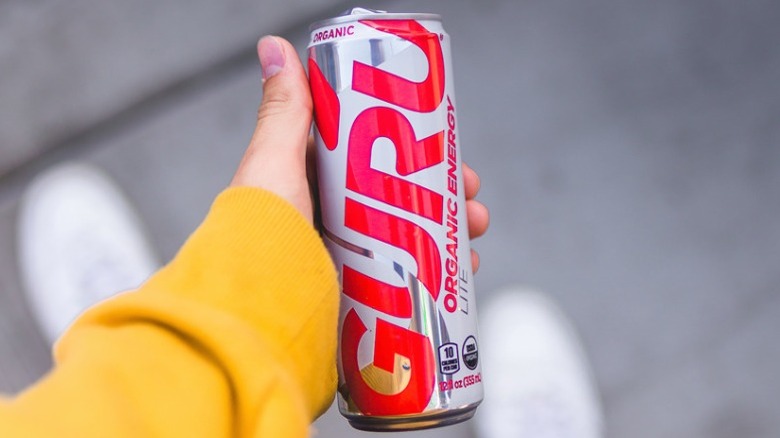 Person with yellow shirt holding a can of Guru Organic Energy drink in hand
