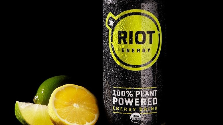 A can of Riot energy drink with sliced lemon and limes next to it