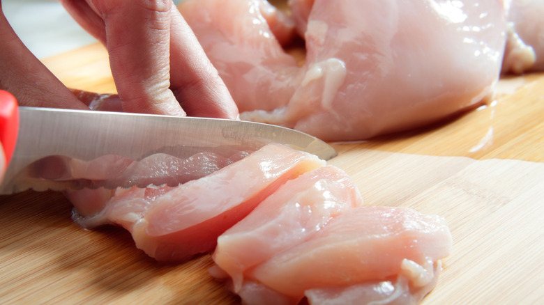 close up silver plate of hand slicing raw chicken