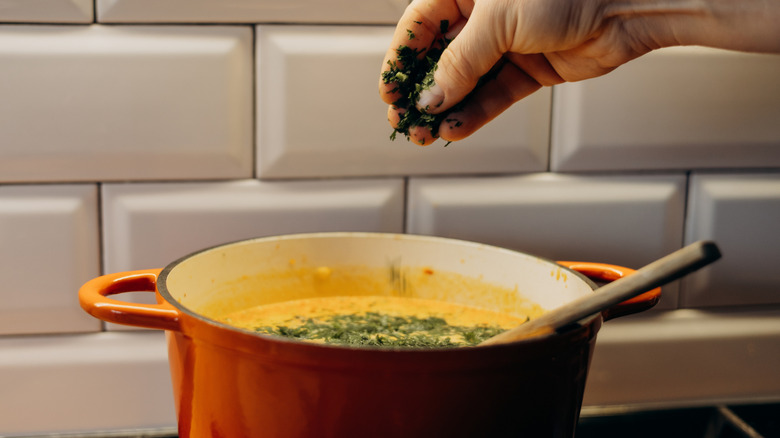 A hand adding chopped parsley to a pot of soup cooking on the stove