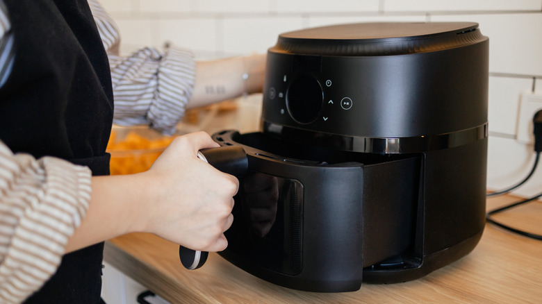 An elegant black air fryer, with a person pulling out the basket