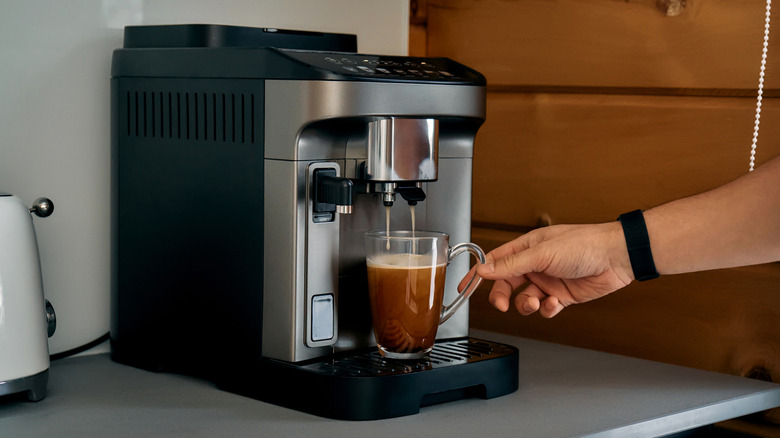 Coffee maker dripping coffee into a glass mug, with a hand reaching for it