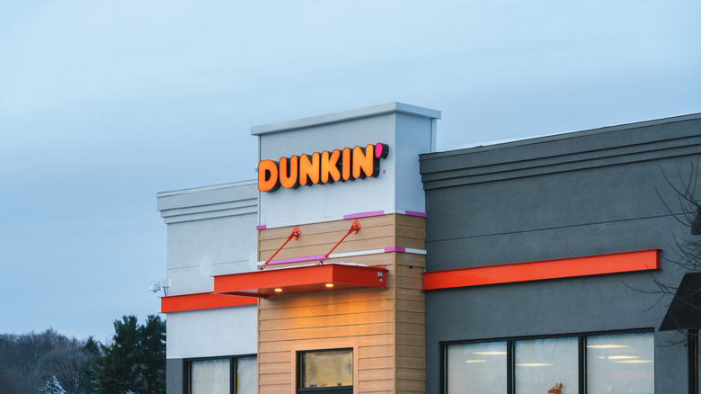 Dunkin' restaurant with illuminated sign against grey sky