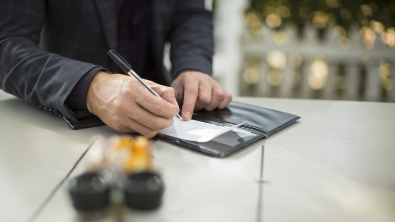 Close-up of unrecognizable man leaving tip on credit card receipt at restaurant
