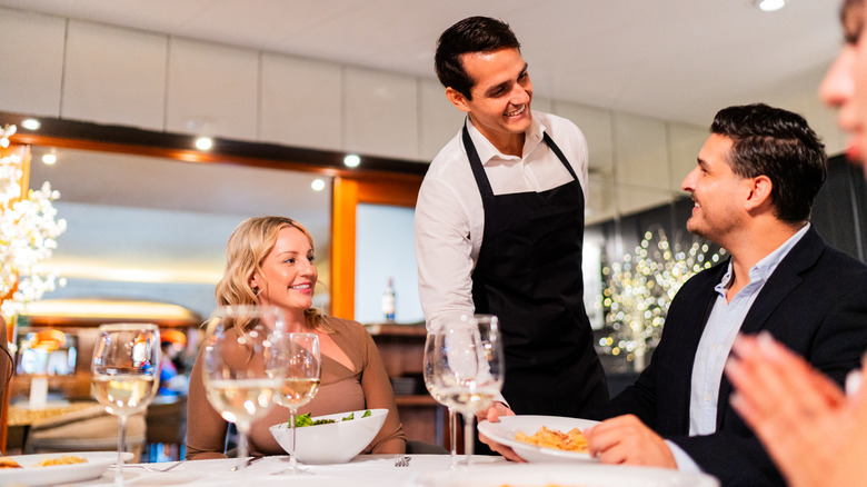 three people at a fine dining restaurant, a waiter in a black apron and white shirt serving a man food