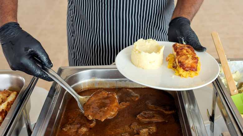aproned worker serving meat in gravy with mashed potatoes and other foods