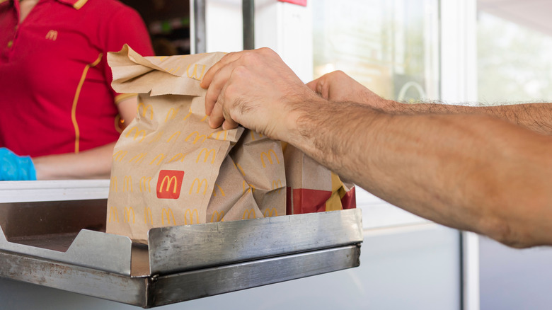 Person picking up two McDonald's paper bags from the drive-thru tray