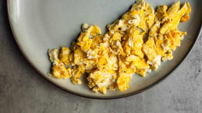 Scrambled eggs sitting on a gray plate on a gray table top