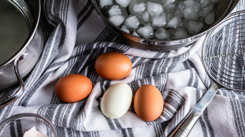 Hard-boiled eggs on towel near a bowl of ice water