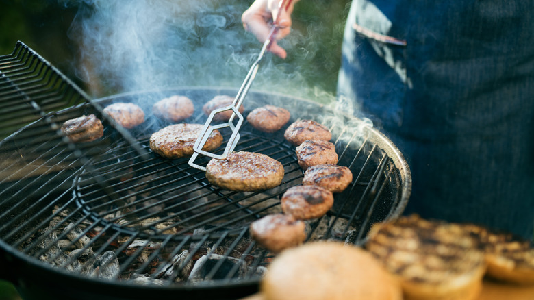 Someone flipping burgers on a charcoal grill on a sunny day