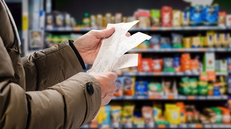 person looking at receipts in front of grocery shelves