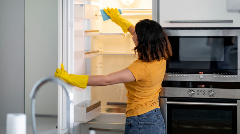 Woman wearing yellow gloves cleans an empty fridge