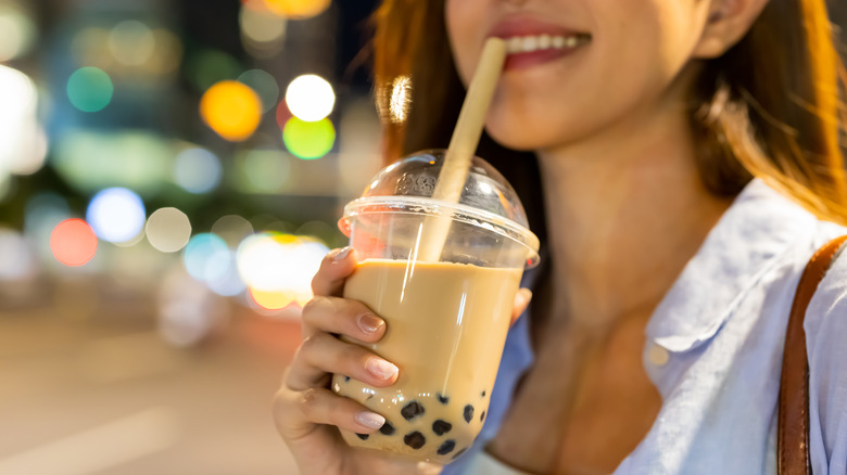 A smiling woman holding a cup of boba with a straw