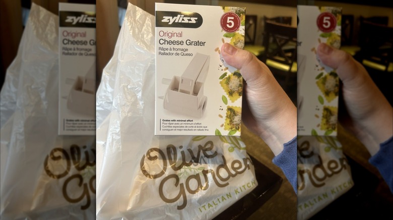 A person holding a box containing a Zyliss Original Cheese Grater in front of an Olive Garden bag