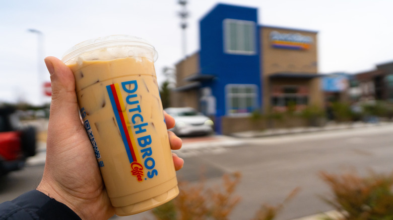Someone holding a small cup of Dutch Bros in front of a store