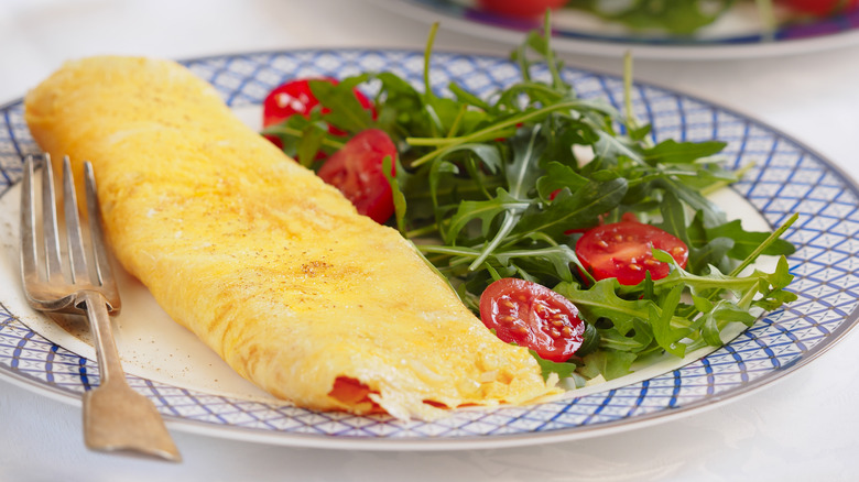 A rolled omelet on a plate accompanied by salad and a fork