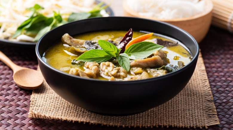 a bowl of Thai green curry garnished with Thai basil
