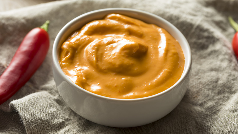 Orange spicy cheese sauce in white ramekin on beige cloth