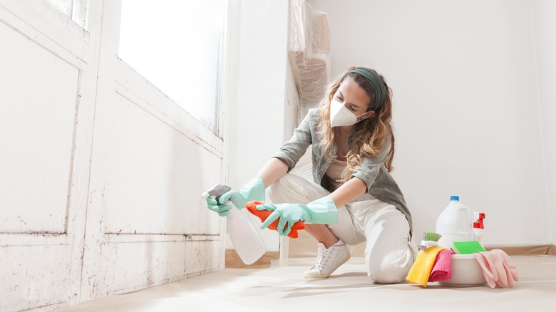 A woman wearing a mask and gloves while cleaning dirty walls