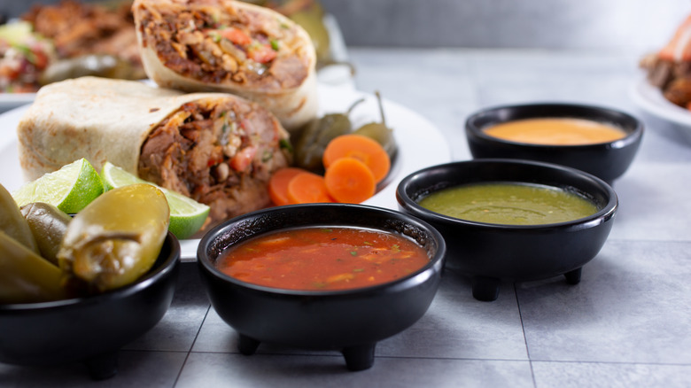 Different salsas in front of a plate of burritos