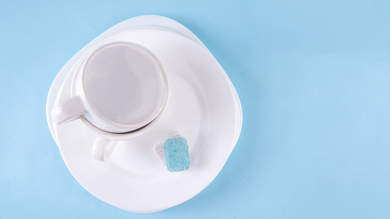 White mugs and saucers next to blue and white dishwasher tablets