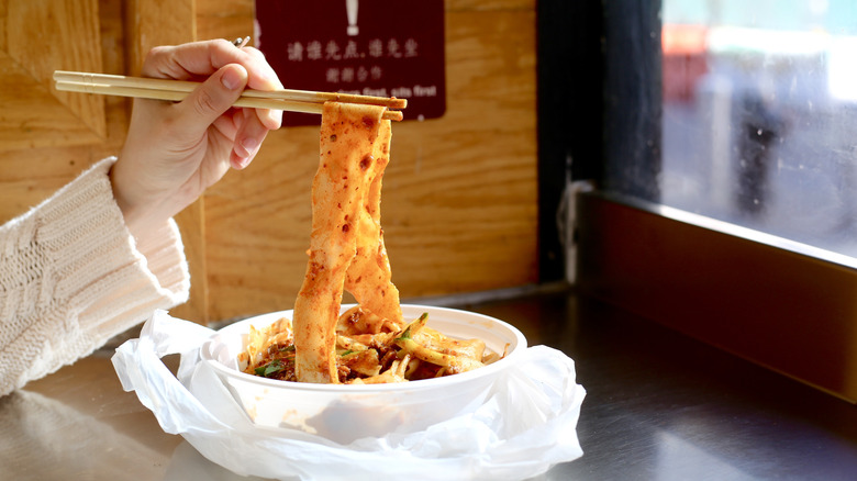 Hand using chopsticks to hold up noodles at a restaurant counter