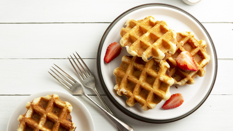 A plate of waffles with strawberries and two forks