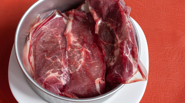 Closeup of thawing raw steaks in bowl with cold water