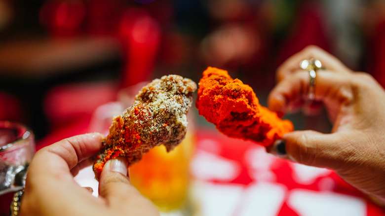 Two hands holding different types of chicken wings clinking them together as though making a toast