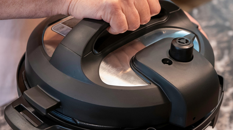 A hand holds the handle of an Instant Pot lid