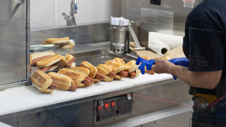 A Costco employee prepares multiple hot dogs