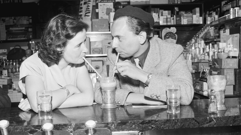 Two people sharing a milkshake at a 1950s ice cream parlor