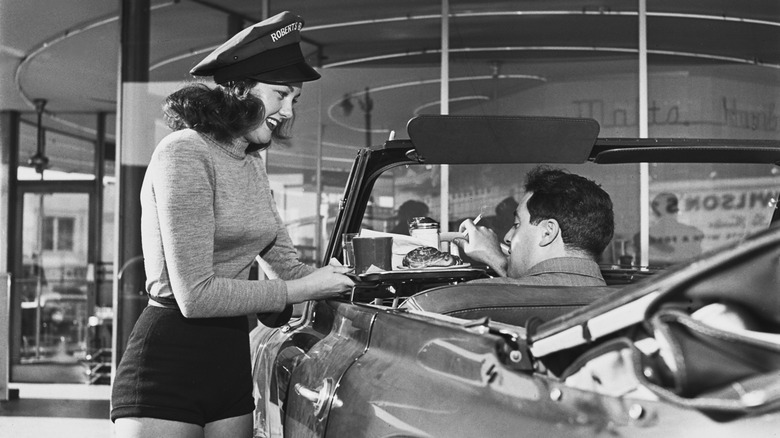 Carhop bringing a tray of food to a man in a convertible 1950s