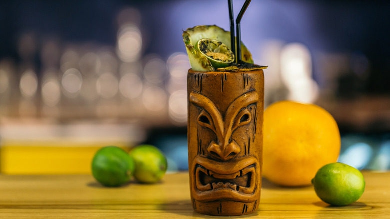 Tiki mug on a bar with limes and pineapple