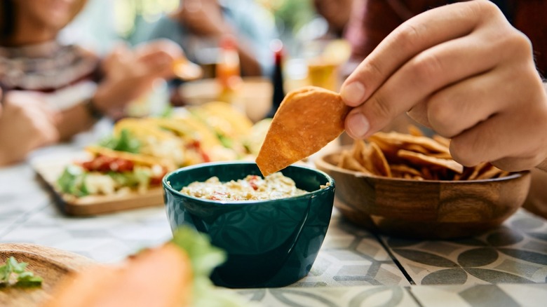 A hand about to dip a homemade tortilla chip in a bowl of guacamole
