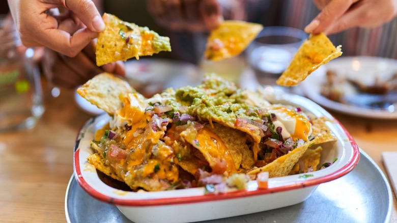 Multiple hands taking nachos from a loaded nacho tray
