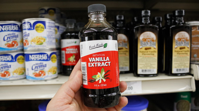 hand holding a bottle of imitation vanilla extract in front of grocery store shelves