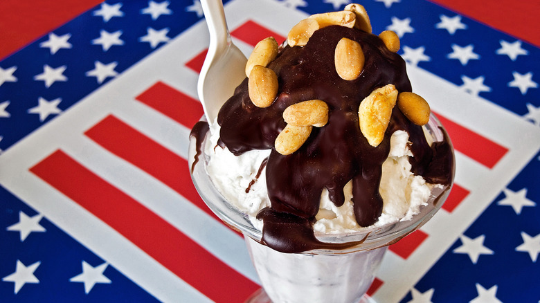 An ice cream sundae covered in peanuts and hot fudge with an American flag background