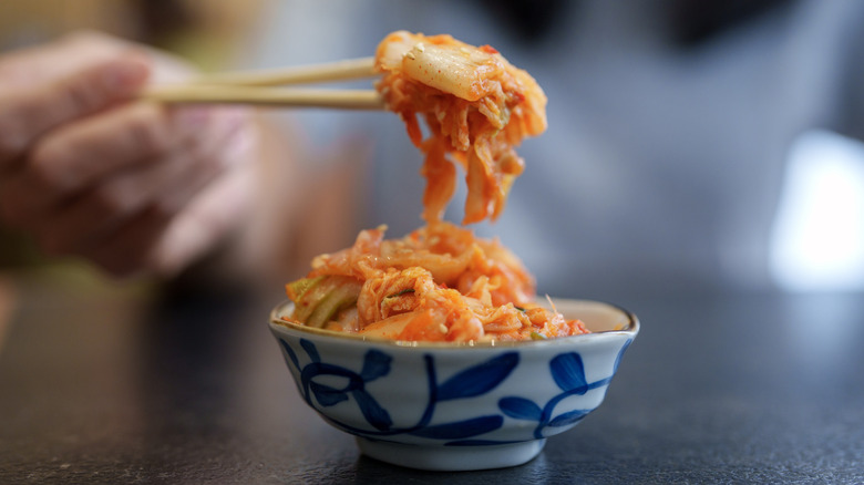 Someone using chopsticks to pick up kimchi out of a blue and white bowl
