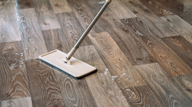 Detail shot of floor cleaning process with soapy water and mop on wood surface