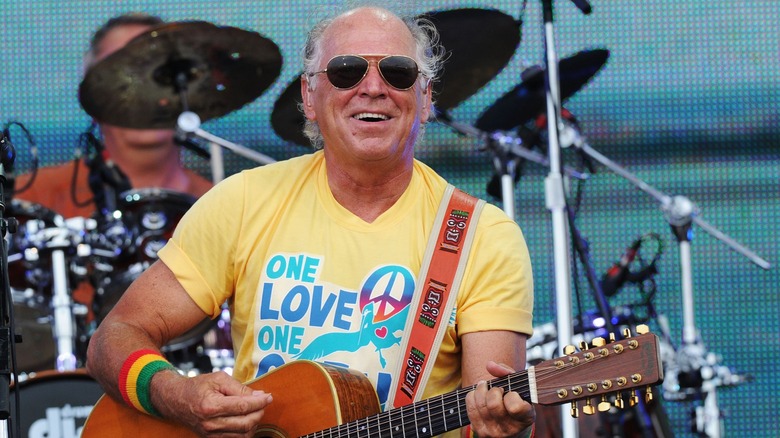 Jimmy Buffett Trop Rocking on stage wearing sunglasses and a yellow tshirt and playing guitar